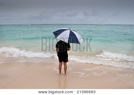 Stojan opálený muž s deštníkem v modré moře pod šedou oblohou