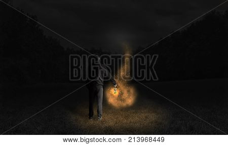 Man holding a lamp and following the fireflies at dark night. Young man in deep forest in magical situation at night with light and old lamp. Old lamp and misty light effect. Man silhouette in dark.