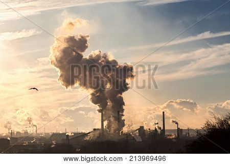 a huge factory. many pipes smoke black smoke in the blue sky. violation of environmental cleanliness. horizontal frame. ecological catastrophy. Apocalypse