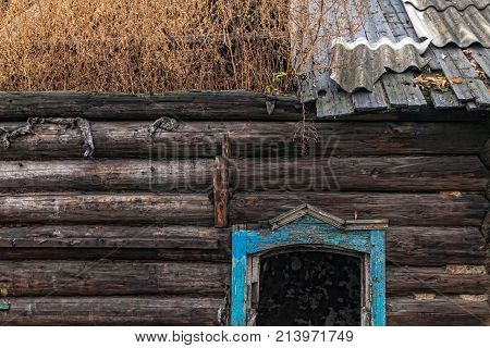 old ruined wooden house close-up. the grass grows on the roof. there are no glasses in the windows. horizontal frame