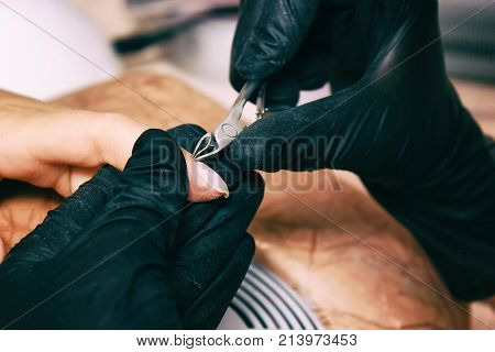 Closeup finger nail care by manicure specialist in beauty salon. Manicurist clear cuticle professional nippers for manicure and pedicure.
