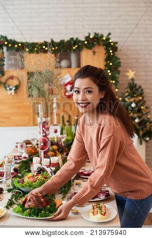 Pretty woman bringing rosated chicken to dinner table