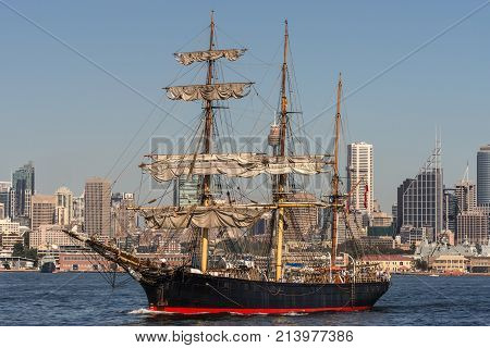 Sydney Australia - March 26 2017: Sailing tall black and red ship with downtown skyline in back ground on blue water and under clear skies.