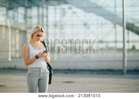 Attractive business woman using a phone and clock while standing in front of windows in an office building overlooking the city