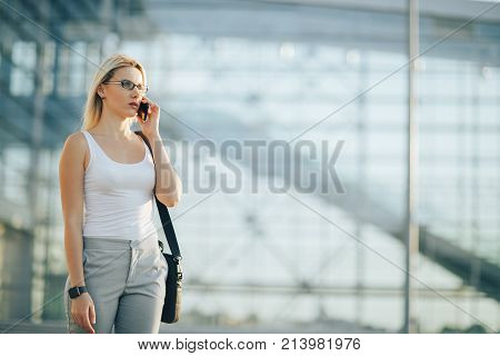 Attractive business woman using a phone and clock while standing in front of windows in an office building overlooking the city
