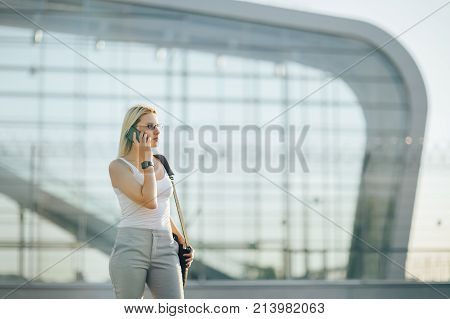 Attractive business woman using a phone and clock while standing in front of windows in an office building overlooking the city