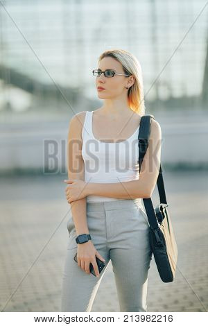 Attractive business woman using a phone and clock while standing in front of windows in an office building overlooking the city