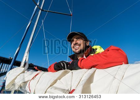 Low Angle View Of Sailor Operating Windlass On Yacht. Working With Ropes And Sail