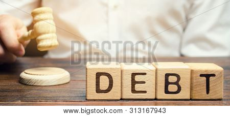 Wooden Blocks With The Word Debt And Judge With A Gavel. The Concept Of Judicial Punishment For Non-