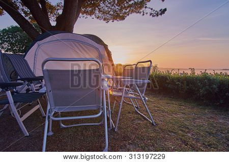 Camping Table With Chairs And A Tent Standing On A Campsite In Front Of A Sunrise In France