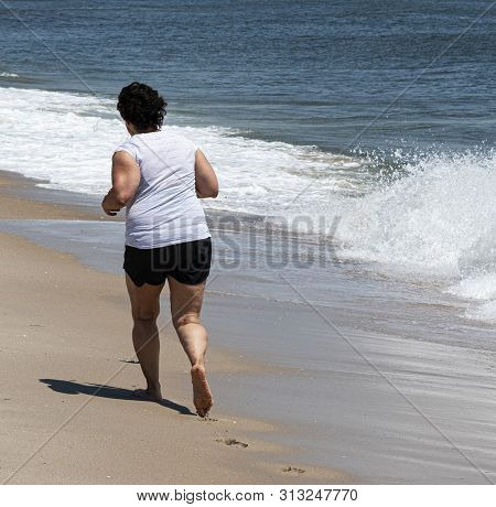 A Women Is Running Barefoot On The Sand Close To The Atlantic Oceean Waters On Her Right Away.