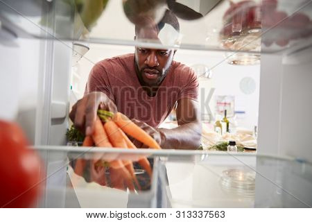 View Looking Out From Inside Of Refrigerator As Man Opens Door And Unpacks Shopping Bag Of Food