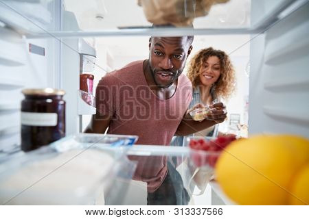 View Looking Out From Inside Of Refrigerator As Couple Open Door And Unpack Shopping Bag Of Food