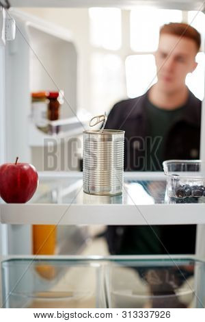 Young Man Looking Inside Refrigerator Empty Except For Open Tin Can On Shelf