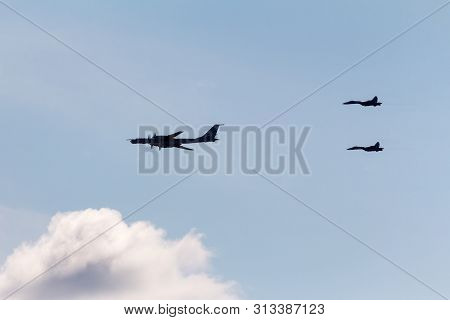 Black Silhouettes Of Three Military Aircraft Flying In The Blue Sky. Two Fighters Escort A Tupolev T