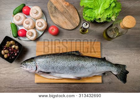 Top View Keta Fish, Whole On The Cutting Board Of The Kitchen Table Next To Olives Tomatoes And Mush