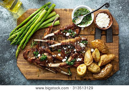 Grilled Lamb Chops With Green Herb Sauce, Feta, Asparagus And Potatoes Served On A Wooden Board