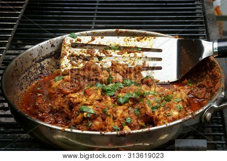 Stirring And Cooking Tava Chicken Outdoors In A Pan On Coals.