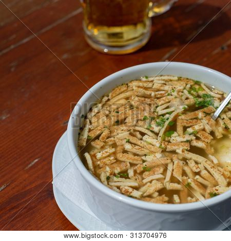 Close-up On Frittatensuppe - Clear Soup With Sliced Pancakes On Wooden Table Accomplaied With A Glas
