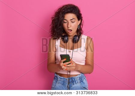 Image Of Impressed Shocked Young Lady Opening Her Mouth Widely With Shock, Looking At Device Screen 
