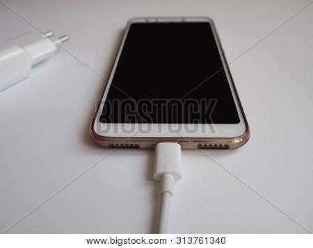 A Smartphone With A White Usb Cable For Charging Close View