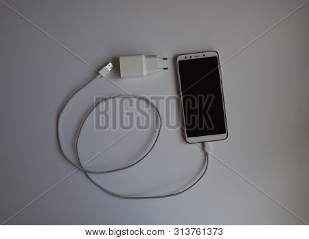 A Smartphone With A White Usb Cable For Charging
