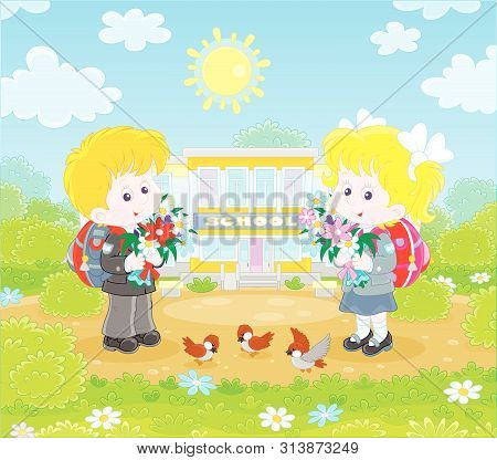 Happy Schoolchildren With Colorful Bouquets Of Flowers And Schoolbags Standing In Front Of Their Sch