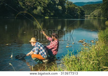 Man Fisherman Catches A Fish. Fly Fishing Is Most Renowned As A Method For Catching Trout Grayling A