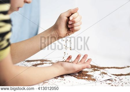 Young Girl Pours Grain Of Flax From One Hand To Another. She Is Going To Add The Grain Of Flax To Th