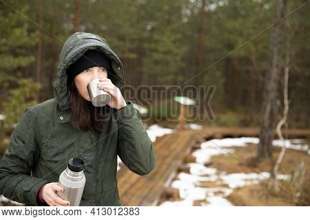 Women Drinks Beverage From Cup And Holds Termos In Other Hand. Resting Taking A Break During Hiking.