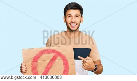 Young handsome man holding prohibited warning banner smiling happy pointing with hand and finger 