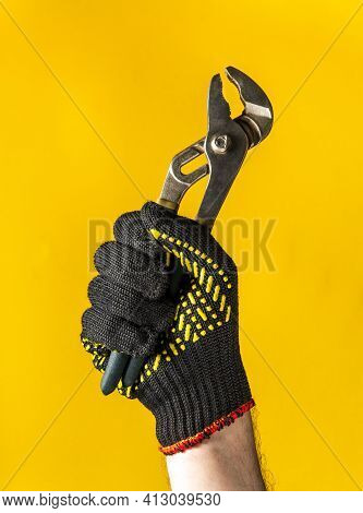 A Raised Hand In Construction Glove Of A Master Plumber Holds Pliers Against Yellow Background. Sign