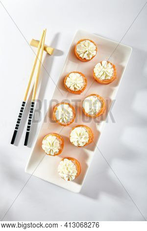 Philadelphia Sushi Roll made with Smoked Salmon. Maki sushi topped with cream cheese. White plate with wooden chopstick on white table. Top view