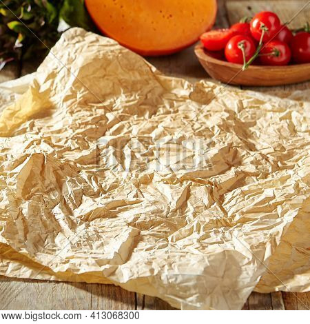 Baking paper with food ingredients. Wooden table at kitchen with baking utensil and fresh vegetables. Crumpled parchment or baking paper as a creative copy space