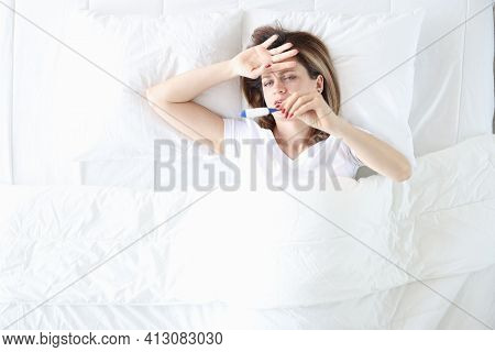 Sick Woman Lies In Bed With Thermometer Closeup