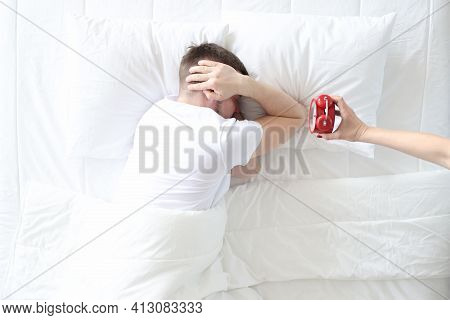 Young Man Covers His Ears With His Hands So As Not To Hear Sound Of Alarm Clock