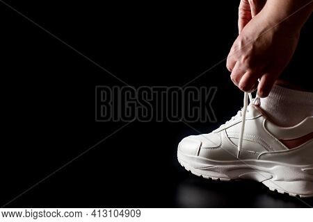 Putting On Sport Sneakers Isolated On Black With Copy Space. Tying Shoelaces On White Sneakers.