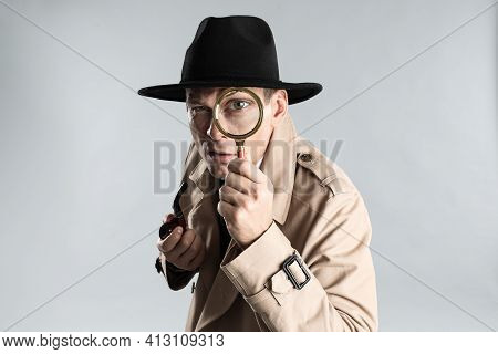 Male Detective With Smoking Pipe Looking Through Magnifying Glass On Grey Background