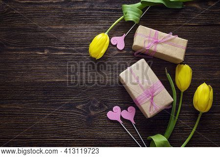 Yellow Tulips With Gift Boxes And Decorative Hearts On Dark Wooden Background. Top View With Copy Sp