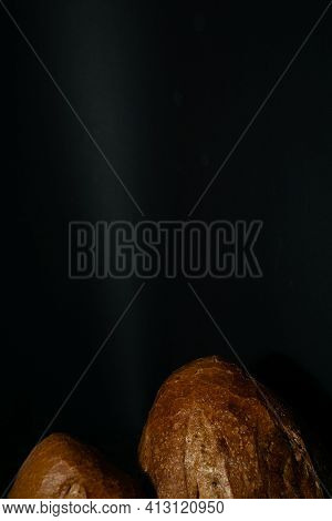 Edge Of Fresh Dark Loaf Of Bread On Black Background. Yeast Product.