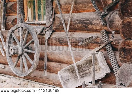 Old Remnants Of Agricultural Utensils Hang On A Wall Of Logs