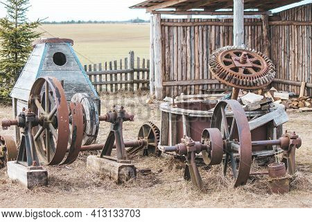Rusty Remains Of Old Agricultural Machinery On The Street Near The Fence