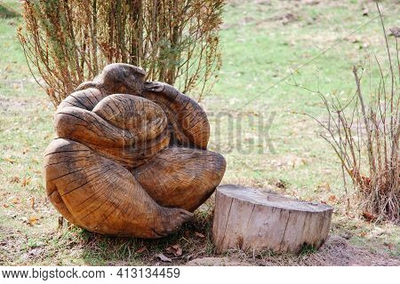 A Figure Of A Pagan Character Made Of Wood Sits On The Ground Next To A Tree Stump