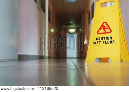 A Sign That Reads Caution Is A Long Empty Industrial Corridor. Yellow Sign Of Slippery Floor In The