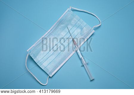Syringe And A Medical Mask On The Blue Background.