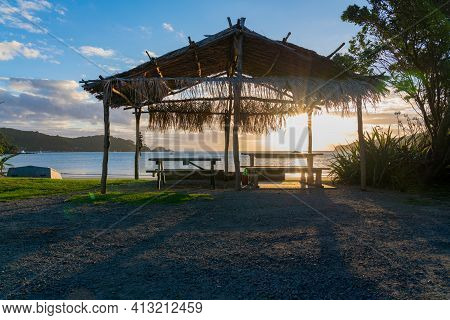 Thatch Roof Shelter On Mulberry Grove Beach Silhouetted Against Golden Sunset On Great Barrier,
