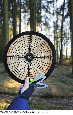 Throwing Knives. Sport And Hobby Concept.throwing Knives Set And Target In Hand On Blurred Forest Ba