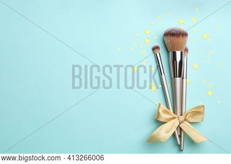 Different Makeup Brushes With Bow And Shiny Confetti On Turquoise Background, Flat Lay. Space For Te