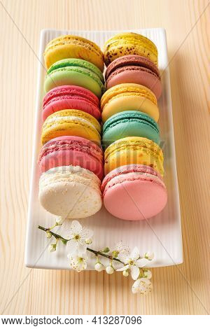 Set Of Multicolored Macaroons And Spring Cherry Blossom Flowers On A White Rectangular Plate Against