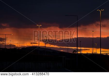 Spectacular Red Sunset With Dark Rainy Clouds Over The Bridge With Silhouettes Of People And Vehicle